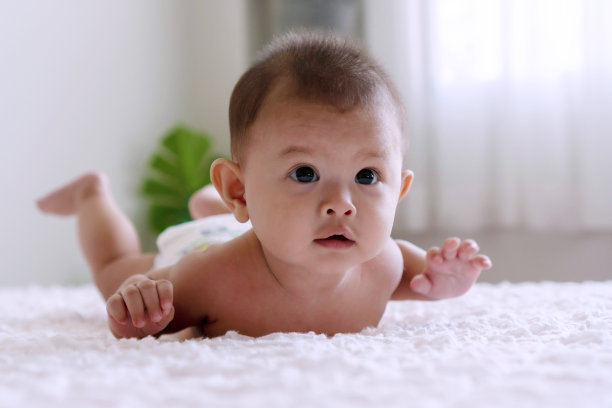 愉快可爱的婴儿躺在白色的床上，放松地看着一些东西或家人。刚出生的小男孩穿着尿布在家里的床上玩。图片下载