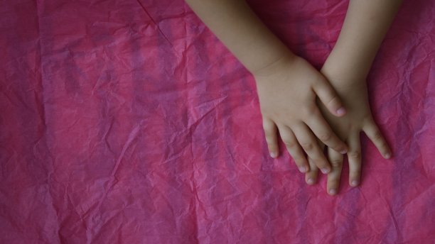 俯视图的孩子交叉的手在粉红色皱巴巴的纸背景与拷贝空间图片下载