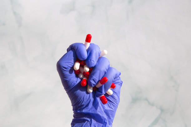 一只戴着蓝色乳胶手套的手抓着满手的药品，维生素胶囊，药品，药物。健康、经营理念图片下载