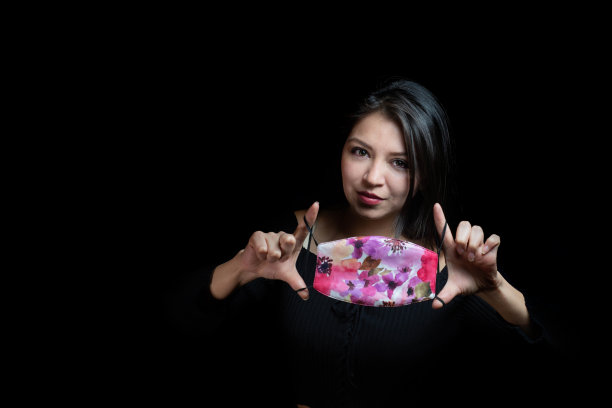 年轻的白人女性拿着一个彩色的面具在一个黑色的背景图片下载