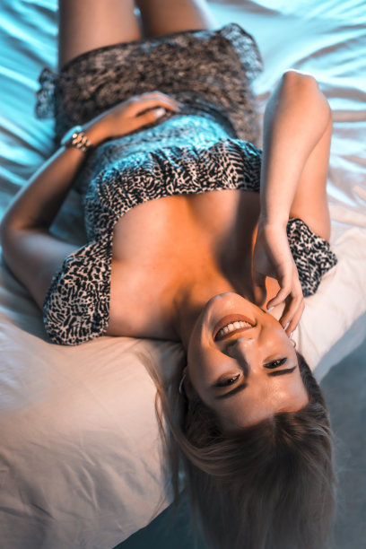 生活方式与一个年轻的金发白种女人在短连衣裙与一个大的黑白领口躺在床上在她的背部。看着微笑，俯冲投篮图片下载