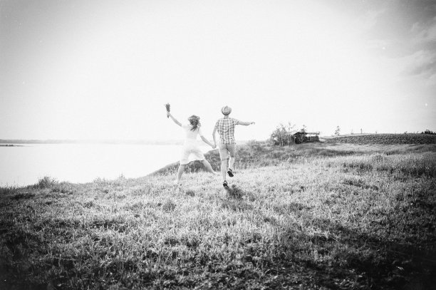 这对迷恋的情侣跑着跳着，在河边的背景下牵着彼此的手。漂亮的女孩戴着花环，时髦的男孩在阳光明媚的日子里花时间在户外。黑白照片图片下载