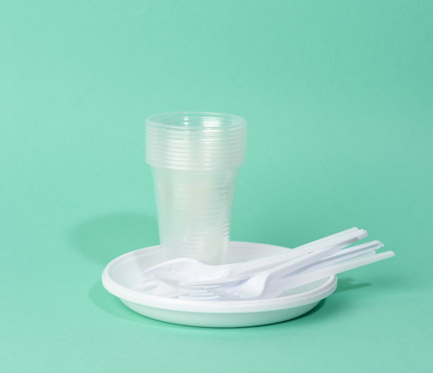 一次性白色塑料餐具盘子，杯子，叉子和刀在绿色的背景图片下载