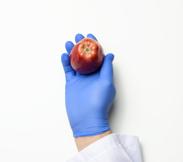 手在一个蓝色乳胶手套拿一个成熟的红苹果在一个白色的背景图片下载