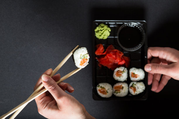 用筷子手挑寿司。寿司外卖盒。吃着黑色塑料盒里的寿司图片下载