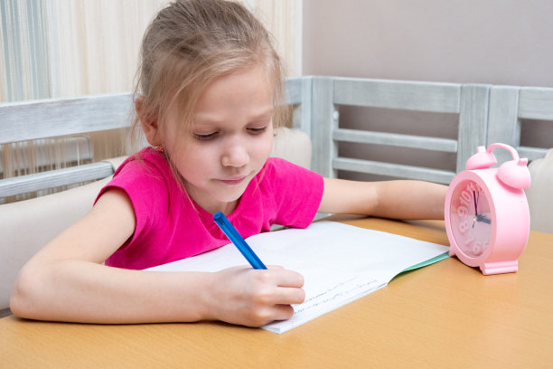 一个小女孩坐在桌子旁，在笔记本上写作业。时间学习。孩子在家里学习。图片下载