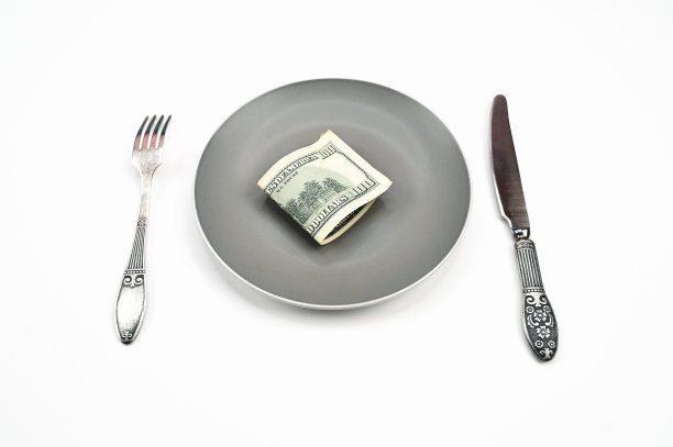百元大钞放在盘子里，叉子和刀放在孤立的白色背景上图片下载