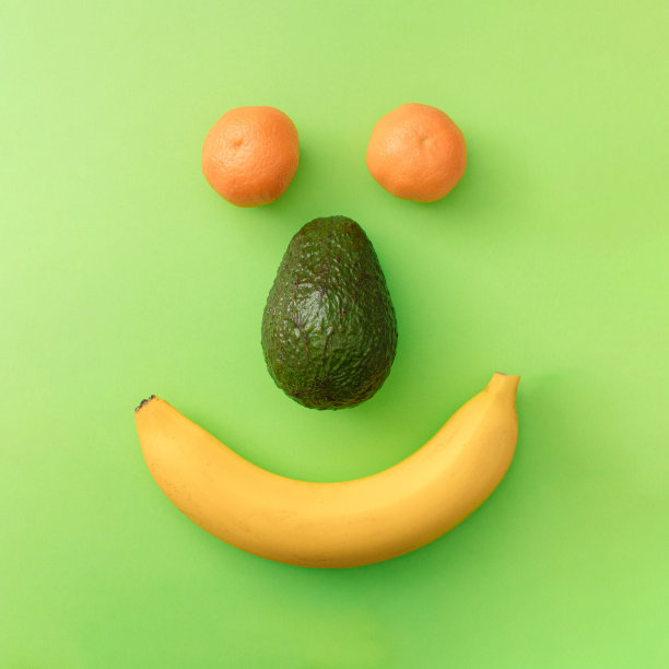 绿色背景上的香蕉、鳄梨和橘子的笑脸。平铺缤纷概念。图片下载