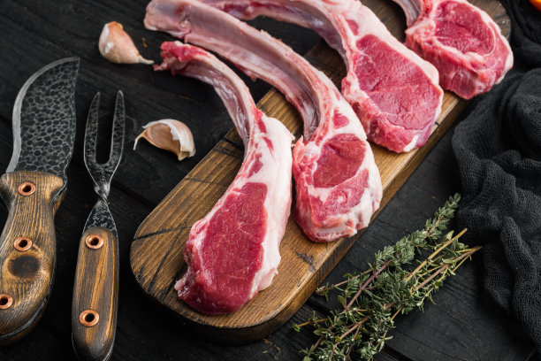生羊排，配料有胡萝卜、橙、香草，放在黑色木桌的背景上素材图片