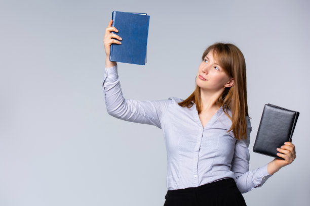身穿灰色衬衫的白人年轻女子，手里拿着两本书。肖像微笑的女商人，教师或大学生，孤立在灰色的背景。图片下载