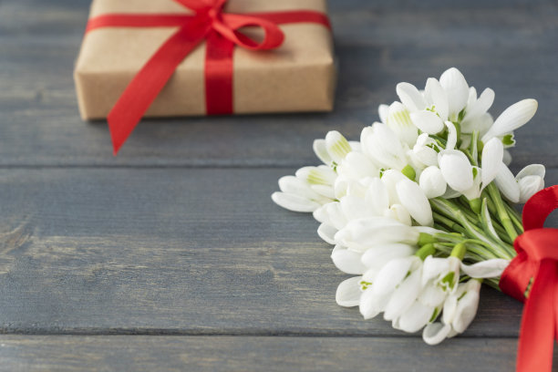 近距离的图片，白色的花莲与红色的丝带，包装的礼盒在黑暗的木制背景。图片下载
