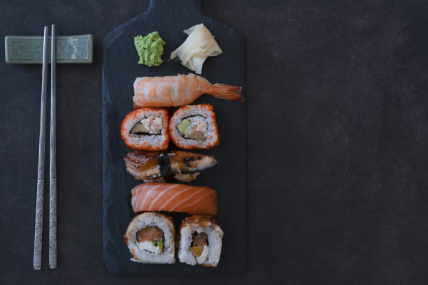 头顶上各种各样的寿司和卷在一个盘子上与hopsticks在黑暗的背景股票照片图片下载