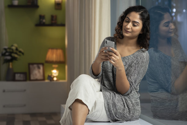 一个年轻女人坐在窗台上，在家里打电话，库存照片图片下载