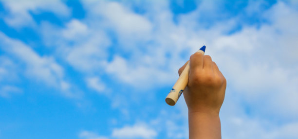 用蓝色铅笔画天空的孩子的手。图片下载