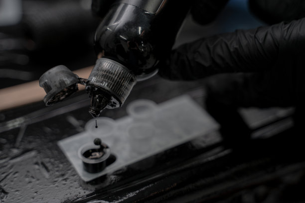 近距离照片纹身大师在黑色手套倒墨水到塑料杯。图片下载