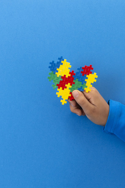 世界自闭症宣传日的概念。孩子手握彩色拼图心在浅蓝色的背景图片下载