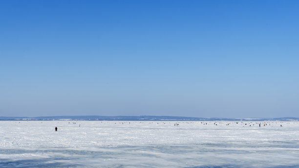 许多渔民冬天在冰冻的湖面上钓鱼在蓝天的背景。休闲活动的概念。空间的文本。图片下载