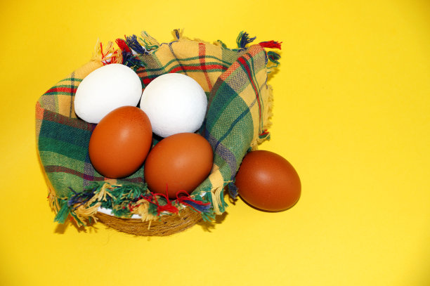 黄色背景的碗里放着方格餐巾，上面放着白色和棕色的鸡蛋和一束绿洋葱图片下载