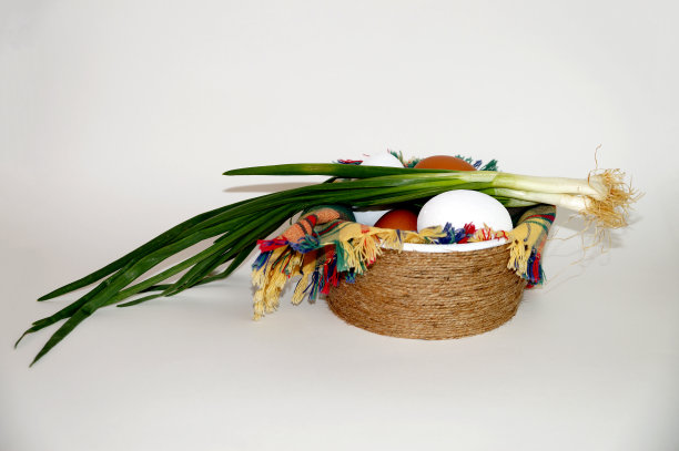 白色背景的碗里放着方格餐巾，上面放着白色和棕色的鸡蛋和一束绿洋葱图片下载