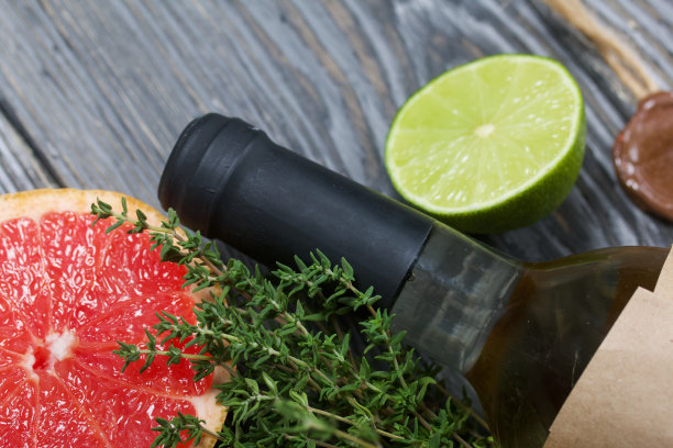 酒精瓶。包裹在纸上。旁边放着百里香，半块酸橙和葡萄柚。松木板。图片下载