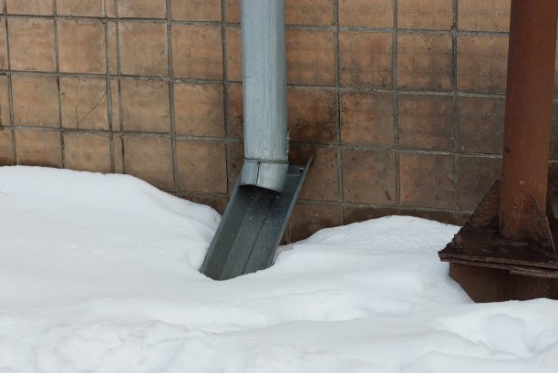灰色的金属排水沟管在一个雪堆上方的棕色墙壁上图片下载