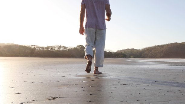 一名男子在日出时走在沙滩上图片下载