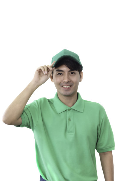 微笑的年轻亚洲男子在绿色t恤制服，持帽孤立在白色背景与clipping路径，服务意识，开朗和热情的概念。图片下载