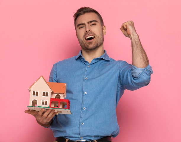 年轻随意的男子举着拳头在空中和展示房子图片下载
