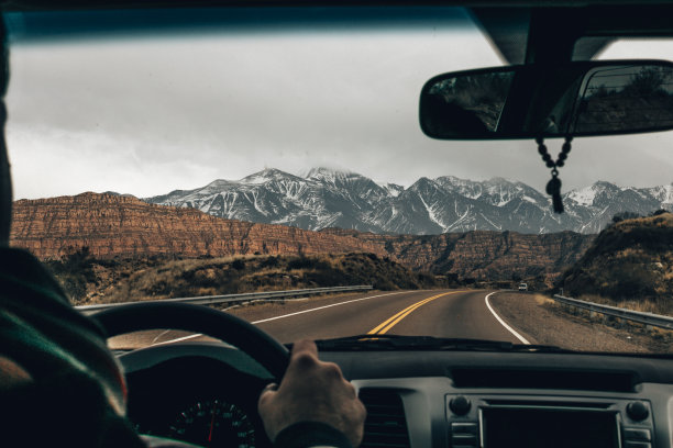 汽车的仪表盘与司机的手在黑色的方向盘上对着移动的冬季沥青道路和美丽的天空图片下载