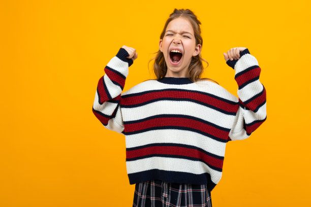 十几岁的女孩在一件条纹毛衣与大张的嘴和举起的手臂呼喊与复印空间的黄色演播室背景的新闻图片下载
