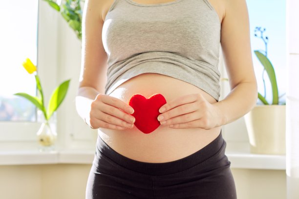 年轻美丽的孕妇肖像显示爱的心与手在肚子上图片下载