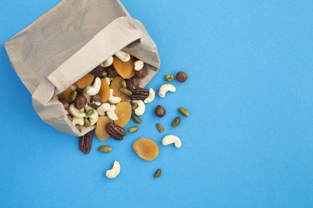 不同的坚果和杏干混合在一个纸袋在蓝色的背景图片下载