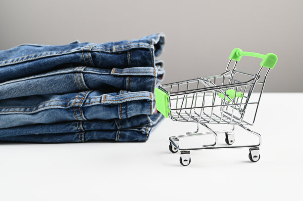 背景是一辆迷你购物车和一堆折叠的牛仔裤。购物和销售的概念。一个基本的，最小的衣柜。网上订购及送货图片下载