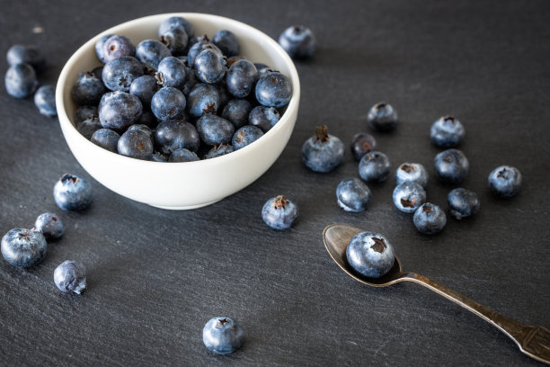 新鲜健康的蓝莓放在一个碗里，散落在黑色的石材台面上。放置你自己的题词图片下载