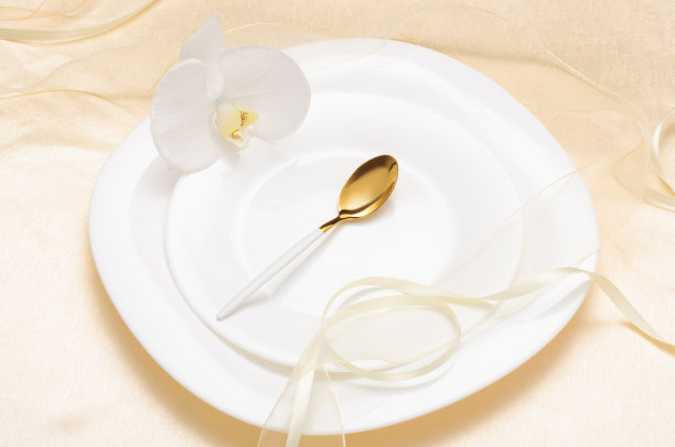浪漫的婚礼餐桌设置在一个浅的背景，金色的勺子在白色的盘子图片下载