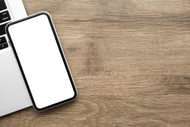 智能手机与空白模拟屏幕是在木桌子上的笔记本电脑。俯视图，平放。图片下载