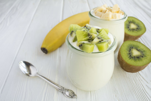 白色的木制背景上，玻璃罐里放着奇异果和香蕉的天然牛奶酸奶图片下载