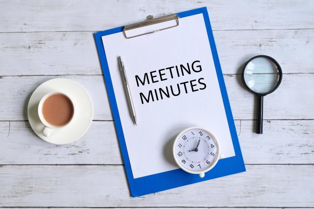 顶部视图的剪贴板与纸写的“会议记录”与放大镜，钢笔，桌子时钟和一杯咖啡在白色的木制背景。图片下载