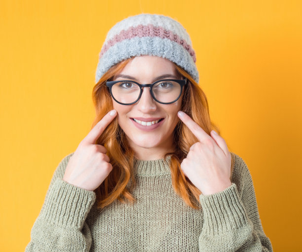 微笑的年轻女子显示她的脸颊和牙齿，孤立在黄色的背景。微笑的漂亮女孩打手势图片下载