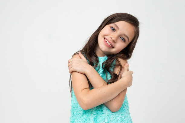 美丽的少女在蓝色的裙子拥抱自己在一个白色的工作室背景图片下载