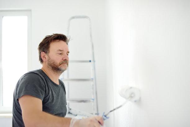 一个成熟英俊的男人正在公寓里修理。那个人用滚筒把墙刷成白色。做你自己。DIY图片下载