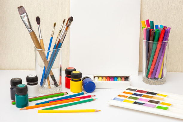 白色桌子上放着画笔和彩色绘画用品。模拟了图片下载