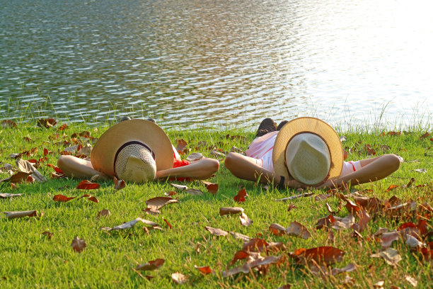 一对戴着宽边帽的夫妇并排躺在阳光明媚的海滨图片下载