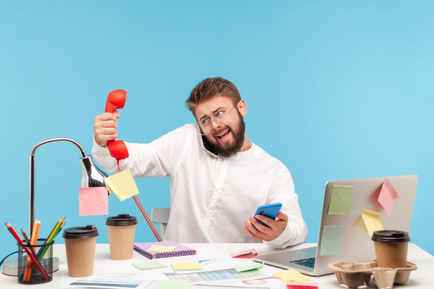 一个忙碌过度工作的人坐在工作场所，手里拿着三部手机，拿着便利贴，接听电话，服务中心图片下载