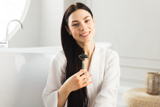 美丽的女孩抱着排水按摩面部滚轮坐在豪华浴室里图片下载