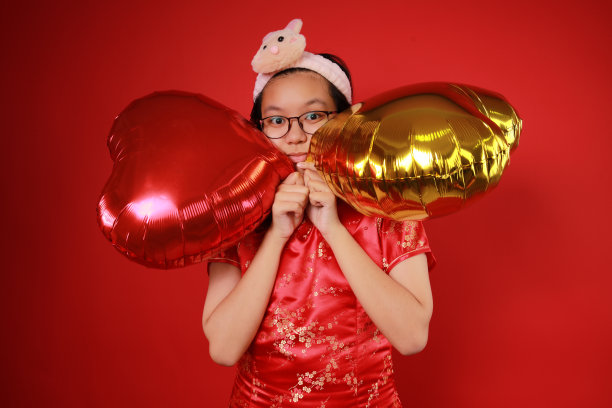 情人节这天，一个女孩在红色背景下玩心形气球图片下载