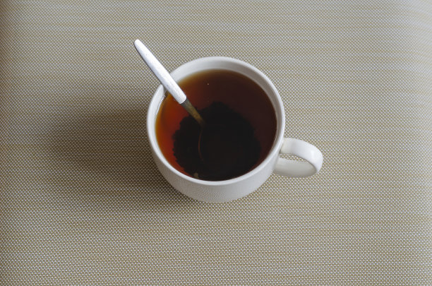 一个白色的陶瓷杯子，里面装满了红茶和一个金属勺子。图片下载