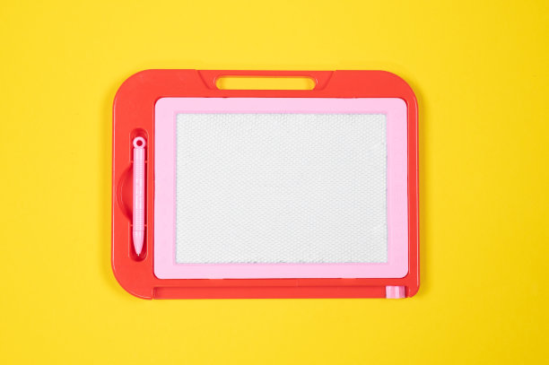 红粉色塑料磁性画板在黄色的桌子上。儿童教育玩具概念图片下载