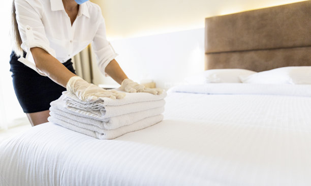 一个女人戴着保护面罩和手套在酒店工作，并为新客人准备枕头库存照片图片下载