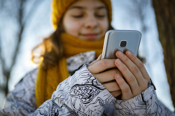 十几岁的女孩戴着温暖的帽子和智能手机图片下载